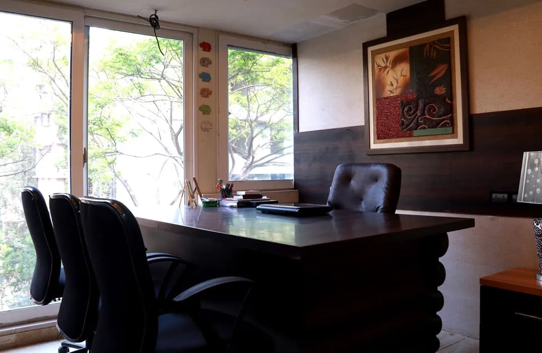 A consultation room at Mindsight Clinic, Malad West, Mumbai, with a wooden desk, chairs and a window onto trees